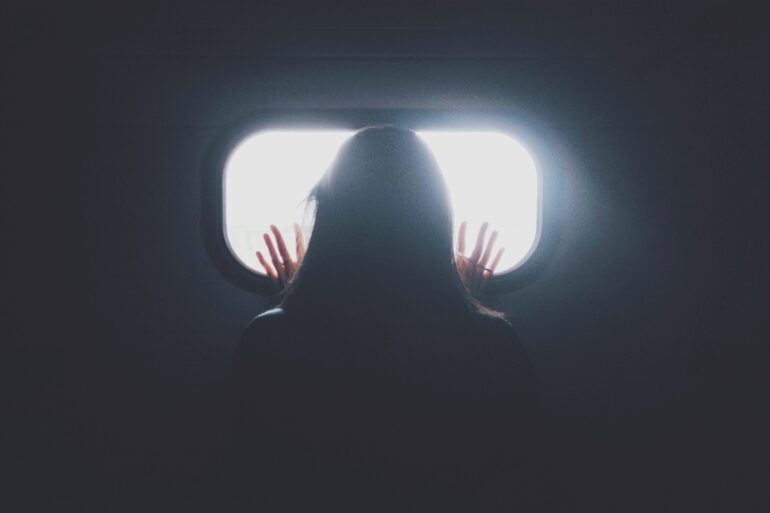 A woman in a dark room looking through a small, bright window